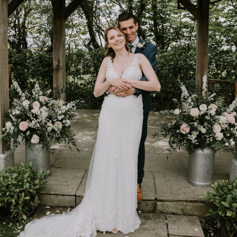 A handsome groom and beautiful bride under an arbor of gorgeous flowers designed by Artem Florum