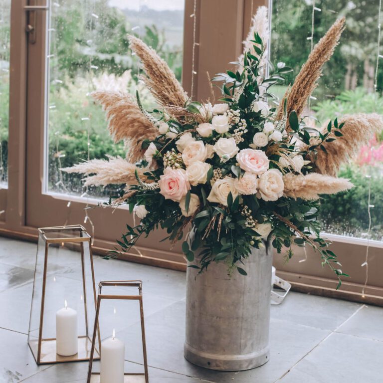 A rustic milk churn filled with summer flowers in a wedding display created by Artem Florum